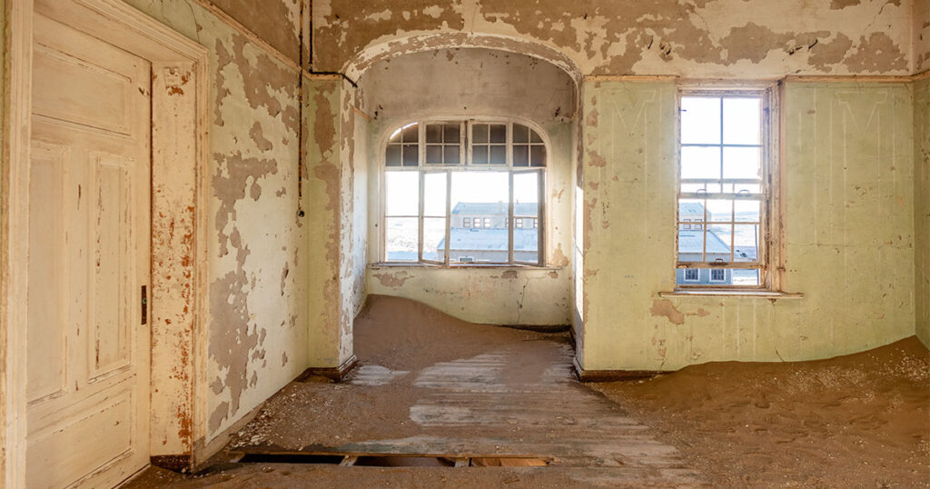 a light green room with an arched doorway that leads to a window that looks out onto a ghost town.