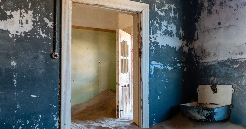 a blue room with the door ajar frozen in sand and a sink hanging from a wall