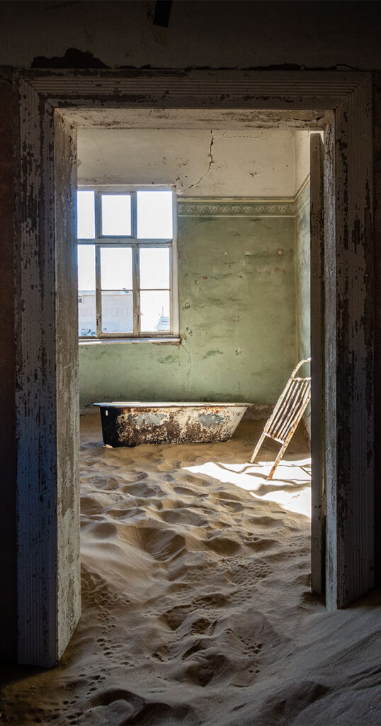 looking thru a doorway that reveals a bathtub and part of a bed frame with a sand filled floor
