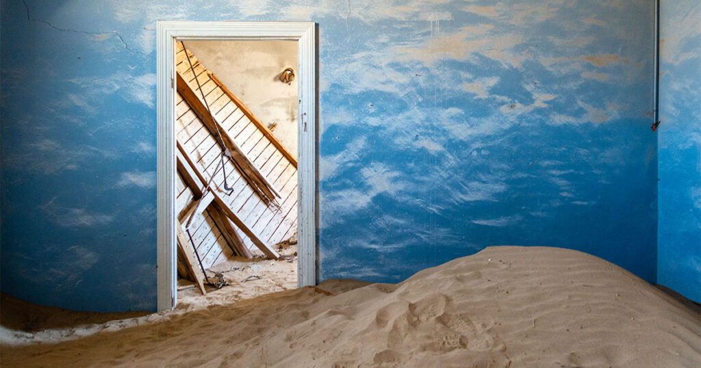 room with sand on the floor blue walls and a doorway that shows wreckage